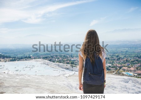 An unknown girl stands with her back standing on a rock looking at the landscape of mountains under a blue sky with light cirrus clouds on a bright sunny day. Denizli. Pamukale. Turkey