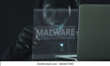 Unknown hacker wearing black mask pulls MALWARE tab from a laptop. Hacking concept