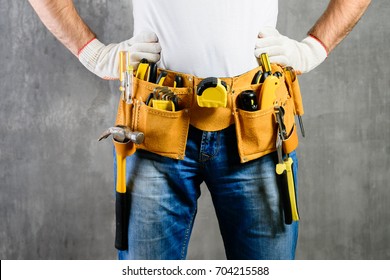 unknown handyman with hands on waist and tool belt with construction tools against grey background. DIY tools and manual work concept