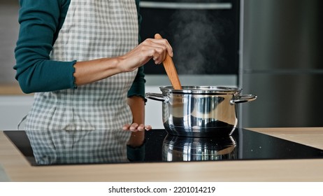 Unknown housewife mistress maid wife mom wears apron prepare food on kitchen surface electric oven cooking aromatic dish boil off soup aromatic borsch by cookery recipe stir porridge with wooden spoon