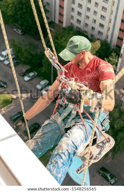 unknown industrial climber in\
dirty uniform works at height. view from the open window building.\
