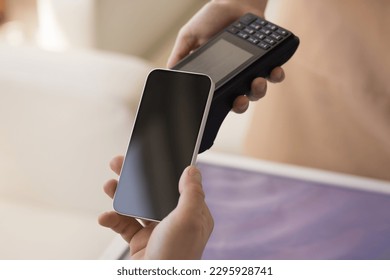 Unknown male client holds modern wireless gadget makes contactless payments by mobile phone, spend money, buy goods, paying bills, purchasing services apply device near terminal machine, close up view