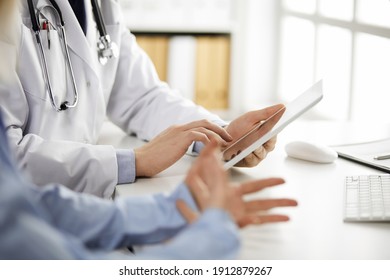 Unknown Male Doctor And Patient Woman Discussing Current Health Examination While Sitting In Clinic And Using Tablet Computer, Closeup Of Hands. Medicine And Healthcare Concept