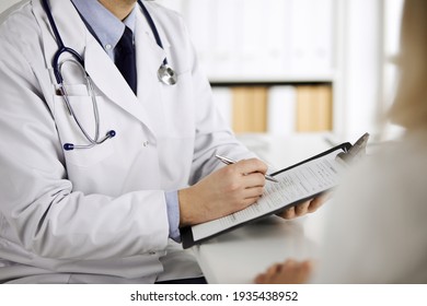 Unknown male doctor and patient woman discussing current health examination while sitting in clinic and using clipboard. Perfect medical service in hospital. Medicine and healthcare concept