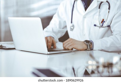 Unknown male doctor sitting and working with laptop in clinic at his working place, close-up. Young physician at work. Perfect medical service, medicine concept - Powered by Shutterstock