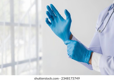 An unknown male doctor wears surgical gloves in a hospital home. The doctor wears gloves over a gray studio background. A doctor who is confident in the care of laboratory coats. - Powered by Shutterstock