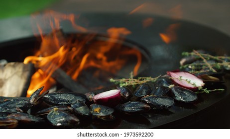 Unknown Man Browning Mussels With Onion And Herbs Outdoors. Closeup Man Chef Cooking Seafood On Barbecue Grill On Backyard. Unrecognized Man Putting Mussels In Shells On Grill Outside.