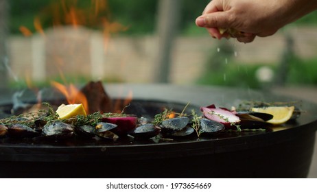 Unknown Man Squeezing Lemon On Seafood On Grill. Closeup Man Chef Cooking Mussels On Grill Backyard. Unrecognized Male Hands Preparing Mussels In Shells With Herbs, Lemon And Onion Outside.