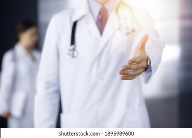 Unknown man-doctor standing straight and offering helping hand in modern clinic. Female colleague is in a hurry at the background of physician. Medicine concept