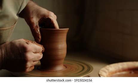 Unknown Master Forming Jar From Wet Clay Piece In Pottery. Unrecognized Clay Artist Modeling Product On Potters Wheel In Workshop. Closeup Man Hands Sculpting In Studio.