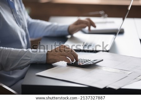 Unknown mature accountant sit at workplace desk working with lot of invoices, financial documents, pay utility bills via e-banking on laptop, close up. Family budget control, bookkeeping job concept