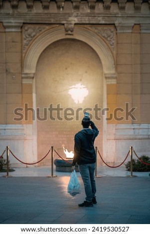 Unknown person taking photo of eternal flame at a small chaplet in the city of Sarajevo at an evening. Flame surrounded by protective fence, lush and fierce flame.