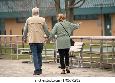 Unknown Senior Couple Holds Hands While Taking A Walk In The Par