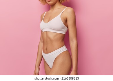 Unbekanntes schlankes weibliches Modell in weißer Unterwäsche zeigt perfekte Körper seidige, gesunde, schlanke Beine tragen weiße Zuschnitte oben und panties einzeln auf rosafarbenem Hintergrund. Torso von Frauen mit flachem Bauch