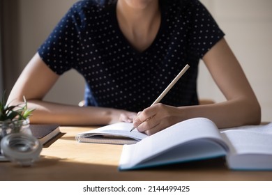 Unknown student girl sit at table with textbook, holds pencil writes essay, prepare for university exams, studying alone indoor, language practice, cram, learns subject, makes chapter overview concept - Shutterstock ID 2144499425