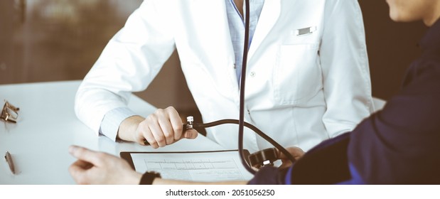 Unknown Woman Doctor Is Checking Her Patient's Blood Pressure While Sitting Together In Clinic. Medicine Concept During Coronavirus Pandemic. Covid 2019