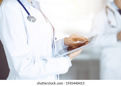 Unknown Woman Doctor Is Checking Some Data At Computer Tablet, Close Up. Young Doctors At Work In A Sunny Hospital. Perfect Medicine And Healthcare Concept