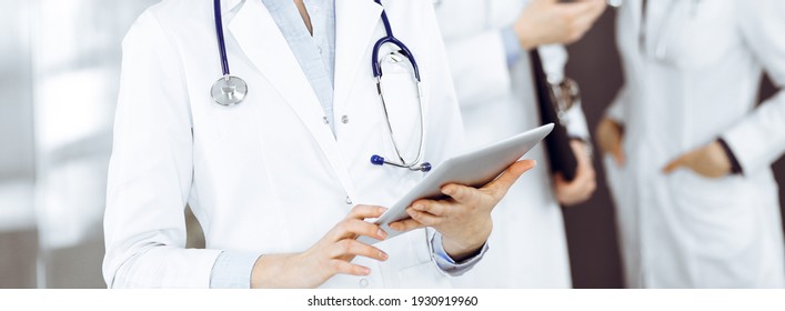 Unknown Woman Doctor Iusing Tablet Computer In Her Hands, While Standing In Clinic. Medicine Concept During Coronavirus Pandemic