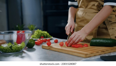 Unknown woman holding a knife in her hands and cutting tomatoes while cooking vegetable salad near kitchen table ,close up - Powered by Shutterstock