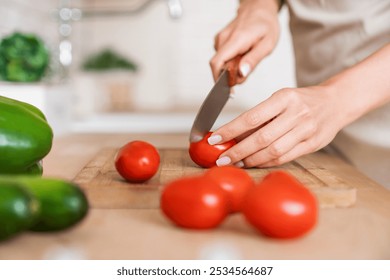 Unknown woman holding a knife in her hands and cutting tomatoes while cooking vegetable salad near kitchen table ,close up. Female hands slicing cherry tomato on wooden board - Powered by Shutterstock