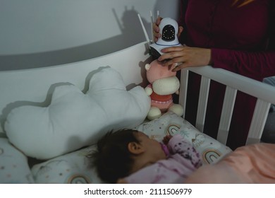 Unknown Woman Mother Adjusting And Setting Up Surveillance Security Camera On Baby Bed At Home In Bedroom Watching Small Child In Cradle While Sleeping In Dark Room At Night