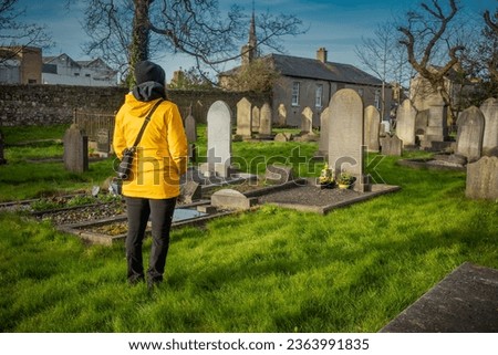 Unknown woman mourning in front of a tombstone in an english looking graveyard. Sad woman paying the last farewell.