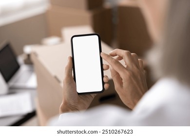 Unknown woman, small business owner, holding smart phone with white mock up screen, close up view over female shoulder. Organizing, scheduling, mobile apps, ordering delivery courier services usage - Powered by Shutterstock