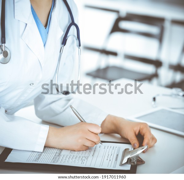 Unknown woman-doctor or internal student filling\
up medical documents while standing in clinic reception desk. Data\
in medicine