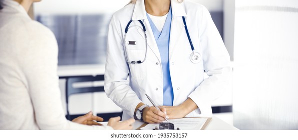 Unknown woman-doctor and patient in hospital. Blonde physician controls medication history records and exam results while using clipboard, close-up. Medicine concept