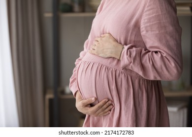 Unknown Young Pregnant Woman In Pink Elegant Dress Standing At Home, Touch Her Big Belly Feeling Love, Advertise Maternity Hospital Or Medical Insurance Cover For Expectant Mother. Pregnancy Concept