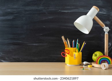 Unlock efficient studying with this student's workplace concept. Side view image displaying lamp and stationery on wooden desk on chalkboard isolated background, offering space for text or advertising