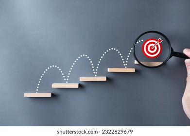 Unlock potential of business success stairs dart and dartboard targets magnifying glass with hand on gray background. Explore opportunities growth embrace steps to achieve ambitions and goal concept.