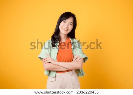 Unlock the power of confidence and well-being with young 30s Asian woman wearing orange shirt. her arm cross gesture on her chest against yellow background, exuding self-assuredness and inner peace.
