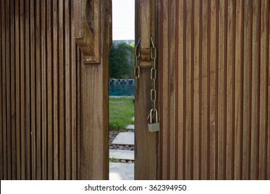 Unlocked metal chain on old wooden doors with green garden and private pool behind.