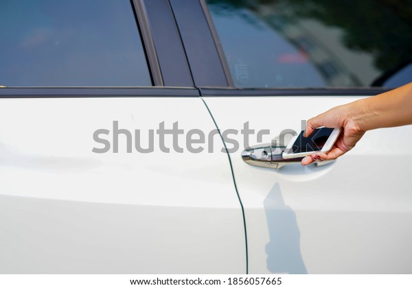 Unlocking Car Using\
Smartphone.New Technology for start car engine. Hand holding mobile\
smart phone to unlock or start car. Technology smart life concept.\
in selective focus.