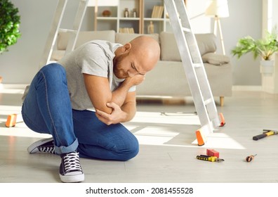 Unlucky Man Who Just Fell Off Ladder Is Sitting On Floor And Touching His Hurt Elbow. Unhappy Guy Who Injured His Arm While Fixing Something At Home Is Feeling Acute Pain In Elbow. Accident Concept