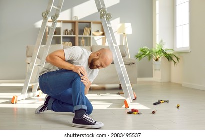 Unlucky Man Who Just Fell Off Ladder At Home Is Sitting On Floor And Hugging His Hurt Knee. Young Guy Who Injured His Knee While Fixing Bad Light Bulb Is Suffering From Acute Pain. Accident Concept