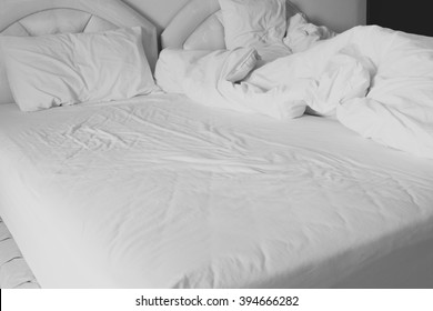 Unmade comfortable bed is strewn with white pillows.