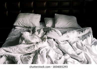 Unmade double empty bed with white linens. Sheets and pillows in the apartment or hotel after a night's sleep. The bed was dirty and unmade. Rumpled blanket in the bedroom