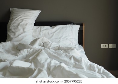 Unmade Sleep Pillows With White Pillowcases And White Blankets On The Bed In Dark Grey Bedroom With Wall Plug Sockets Outlet And Switch. Healthy Sleep Habits, Bed And Breakfast Theme (selective Focus)