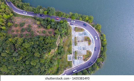 Unmanned Aerial Vehicle (UAV) Overhead Fleet Across U-shaped Highway, Trees And Reservoirs On Both Sides Of The Road