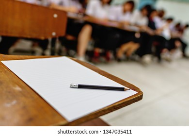 Unoccupied test desk, student absent the test because of sickness, educational concept image of written test room with blurred background of students on the back - blank answer sheet and a pencil - Shutterstock ID 1347035411
