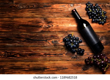 Unopened vintage bottle of red wine with blank matte black label & bunches of ripe grapes on wooden table background. Expensive bottle of cabernet sauvignon concept. Copy space, top view flat lay