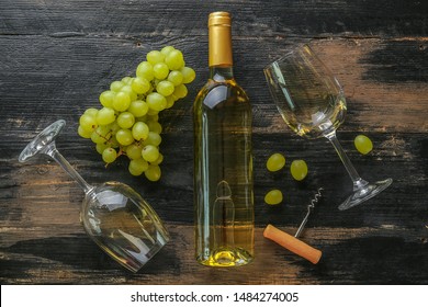 Unopened vintage bottle of white wine without label and bunches of ripe organic grapes on grunged wood table background. Expensive bottle of chardonnay concept. Copy space, top view, flat lay.