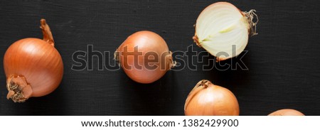 Unpeeled raw yellow onions on a black surface, top view. Flat lay, overhead, from above. Close-up.