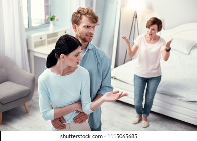 Unpleasant Cohabitation. Unhappy Young Couple Standing Together While Listening To Complains Of The Mother In Law