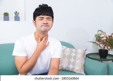 Unpleasant pain. Sad unhappy handsome man sitting on the sofa and holding his neck while having Sore throat.