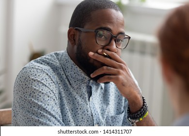 Unpleasantly Surprised African-american Businessman Listening Female Caucasian Coworker With Bad News. Human Resources Generalist Keeping Hand On Mouth Has Ugly First Impression Interviewing Candidate