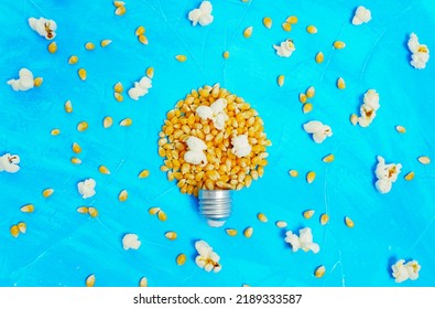 Unpopped And Popped Corns Scattered On Blue, Some Kernels Arranged Into A Lightbulb Shape.