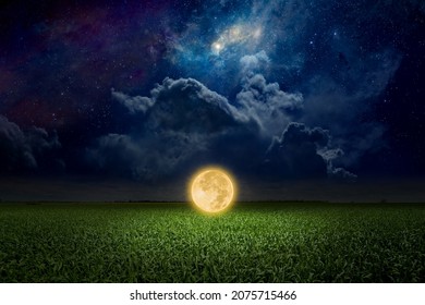 Unreal fantastic image - luminous sphere, similar to full moon, levitates over green field. Bright stars, glowing nebula and clouds in dark blue sky. Elements of this image furnished by NASA - Shutterstock ID 2075715466